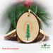 A hand-painted evergreen tree with falling snow on the back of bird wood slice ornaments available for purchase at Cove Creek Photography.